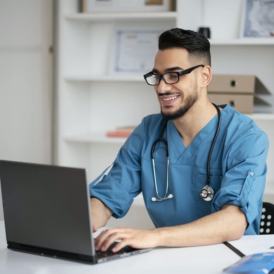 Médico em consultório trabalhando no computador, com a agenda organizada.